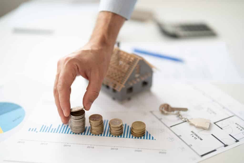 Property management fees in Phuket illustrated by stacked coins, house model, and financial chart showing rental investment growth and cost analysis.