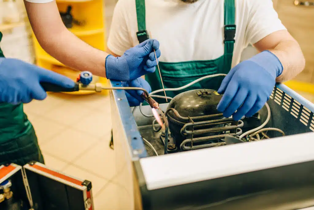 Refrigerator Repair Services in Phuket: Technicians repairing a refrigerator compressor system.